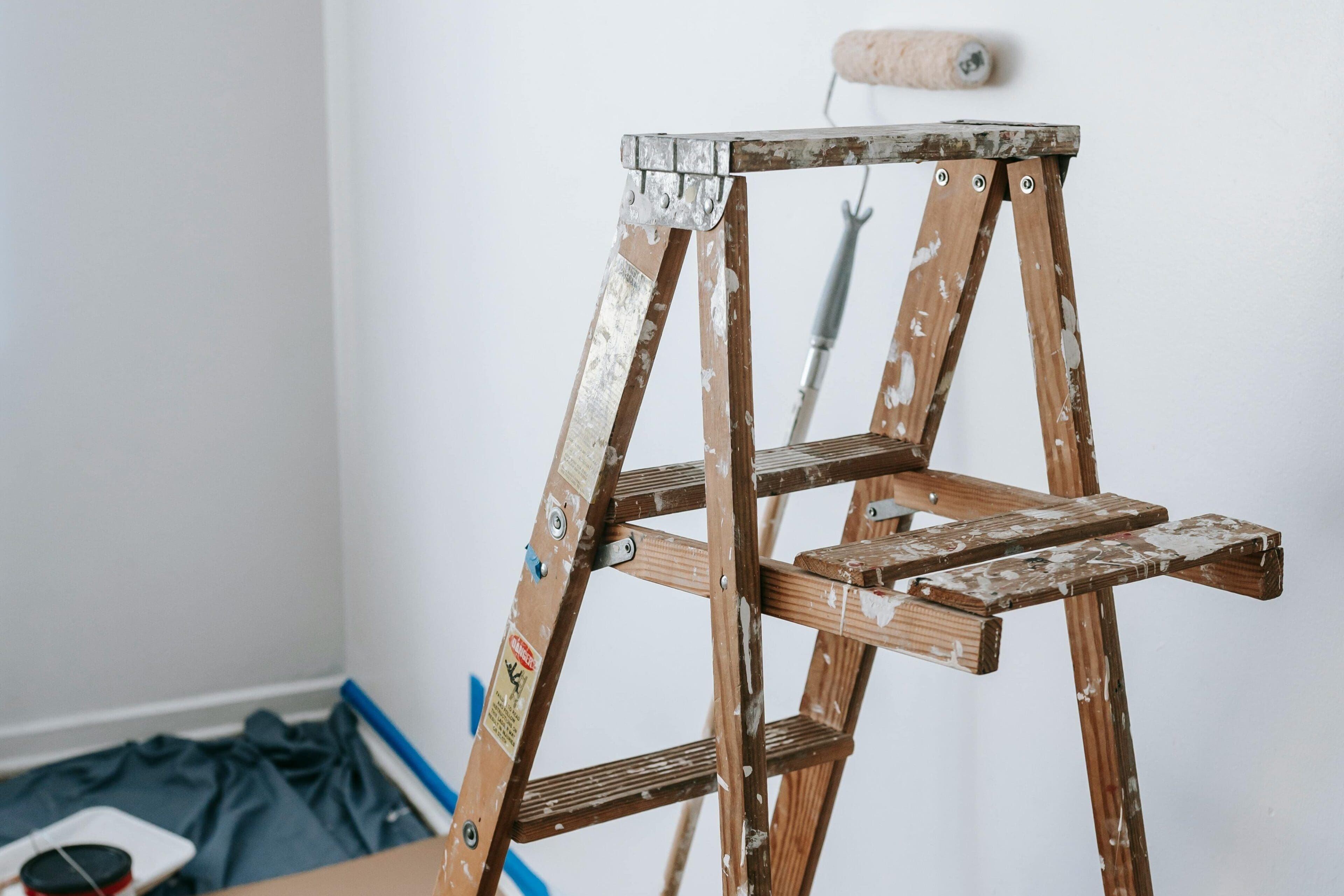 A ladder with paint on it in the corner of a room.